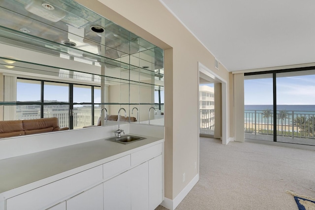 bar featuring white cabinetry, sink, a water view, and light colored carpet