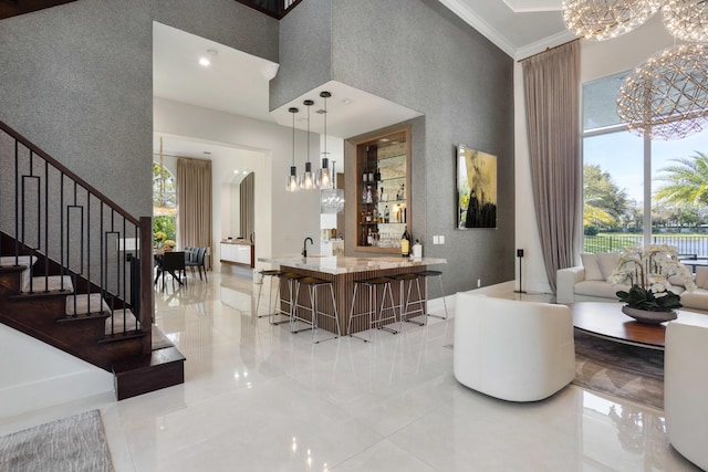 interior space featuring indoor wet bar, crown molding, a notable chandelier, hanging light fixtures, and stairway