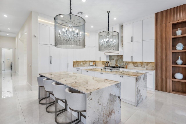 kitchen with decorative light fixtures, tasteful backsplash, white cabinets, a large island with sink, and light stone countertops