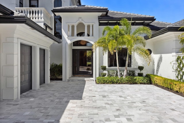 view of exterior entry featuring decorative driveway, stucco siding, a balcony, a garage, and a tiled roof