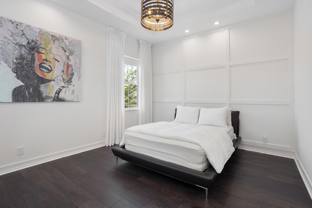 bedroom with baseboards, dark wood finished floors, a tray ceiling, a decorative wall, and recessed lighting