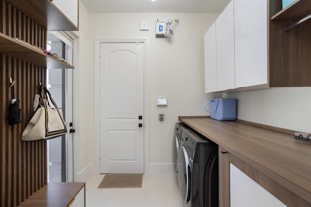 clothes washing area featuring baseboards, cabinet space, washing machine and clothes dryer, and light tile patterned flooring