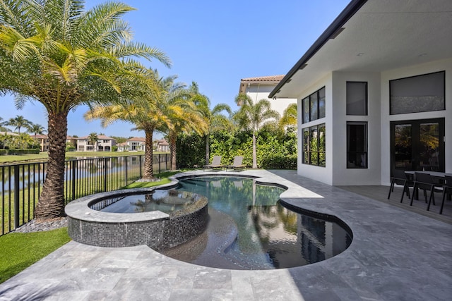 view of pool with a patio, a water view, fence, and a pool with connected hot tub