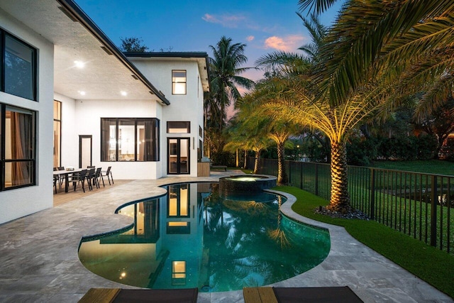 pool at dusk with a patio, a fenced backyard, and a pool with connected hot tub