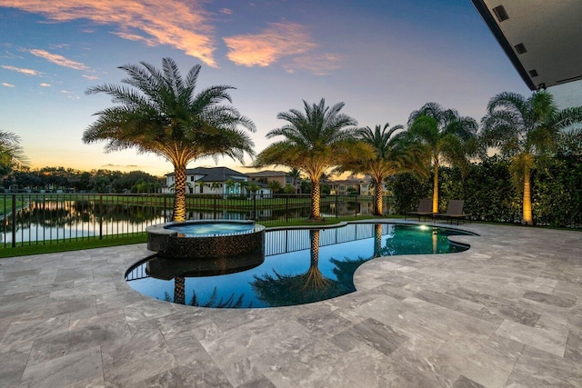 pool at dusk featuring a pool with connected hot tub, fence, and a patio