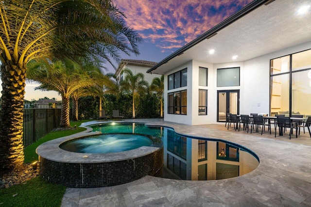 pool at dusk with a patio area, a pool with connected hot tub, and fence