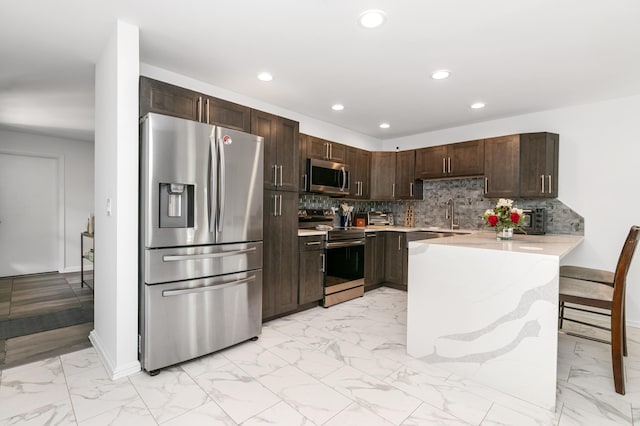 kitchen with kitchen peninsula, appliances with stainless steel finishes, tasteful backsplash, dark brown cabinets, and sink