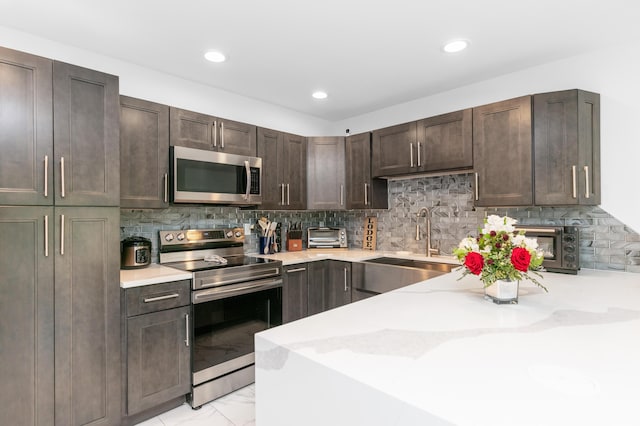 kitchen featuring light stone countertops, backsplash, dark brown cabinetry, stainless steel appliances, and sink