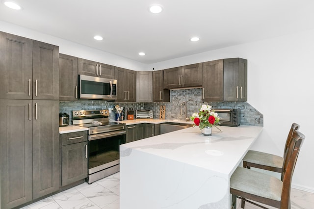 kitchen featuring sink, appliances with stainless steel finishes, dark brown cabinets, kitchen peninsula, and a breakfast bar area