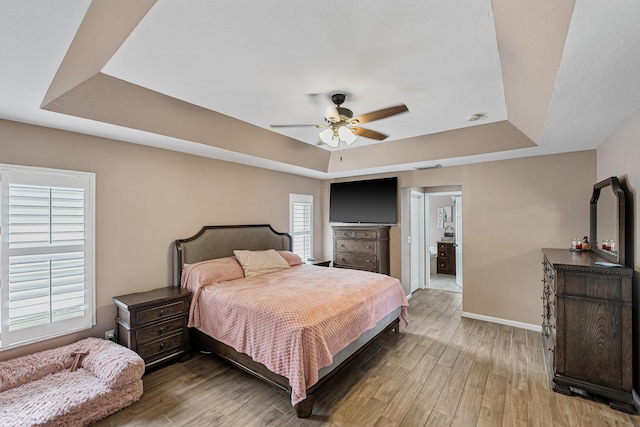 bedroom featuring a raised ceiling, connected bathroom, ceiling fan, and hardwood / wood-style flooring