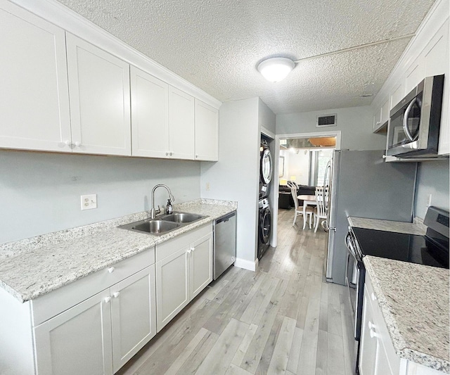 kitchen featuring appliances with stainless steel finishes, sink, light hardwood / wood-style flooring, stacked washer and clothes dryer, and white cabinetry