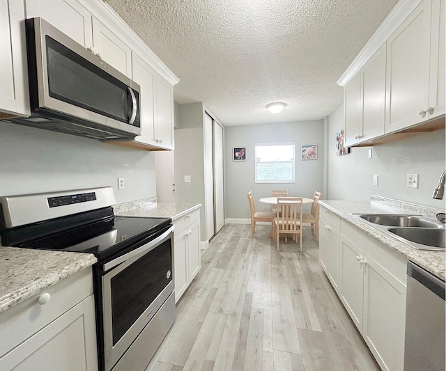 kitchen with sink, white cabinets, light hardwood / wood-style floors, stainless steel appliances, and light stone countertops