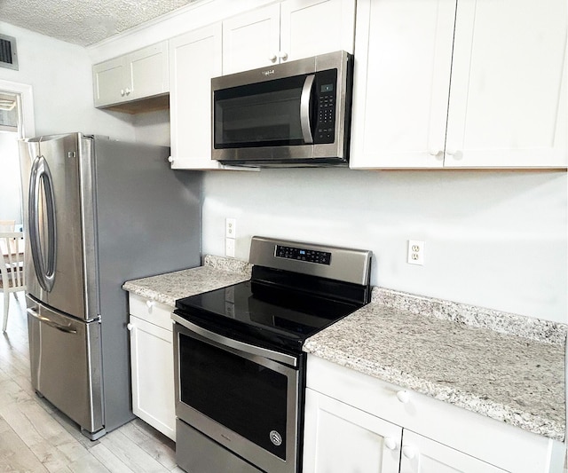 kitchen with light stone counters, stainless steel appliances, white cabinetry, and light hardwood / wood-style flooring