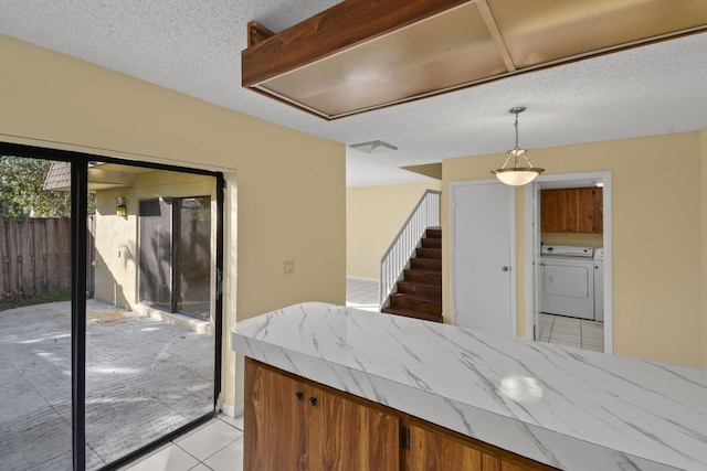 kitchen featuring decorative light fixtures, washer and clothes dryer, a textured ceiling, and light tile patterned flooring