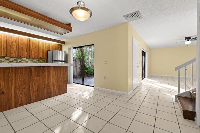 kitchen featuring light tile patterned floors, stainless steel refrigerator, tile counters, a textured ceiling, and kitchen peninsula