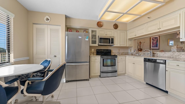 kitchen with light stone countertops, appliances with stainless steel finishes, light tile patterned floors, and cream cabinets