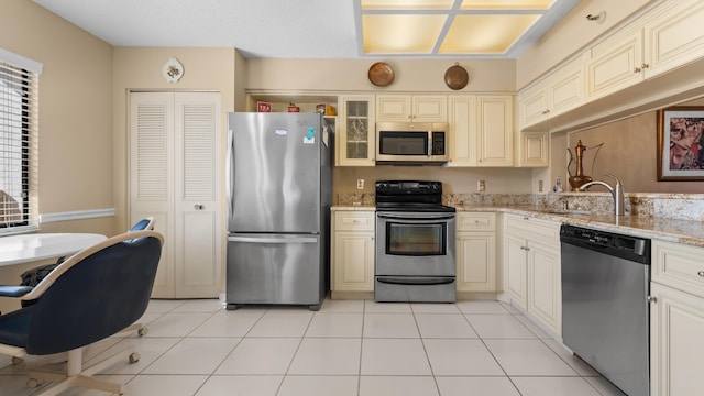 kitchen with sink, light stone counters, cream cabinets, light tile patterned floors, and appliances with stainless steel finishes