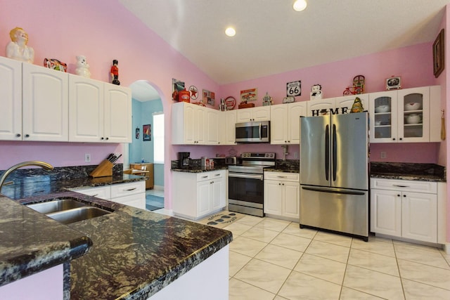 kitchen with glass insert cabinets, arched walkways, appliances with stainless steel finishes, a sink, and lofted ceiling