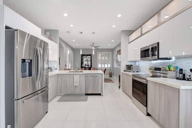 kitchen with kitchen peninsula, appliances with stainless steel finishes, tasteful backsplash, ceiling fan, and sink