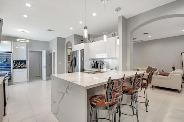 kitchen with white cabinets, sink, decorative light fixtures, stainless steel fridge with ice dispenser, and a breakfast bar area