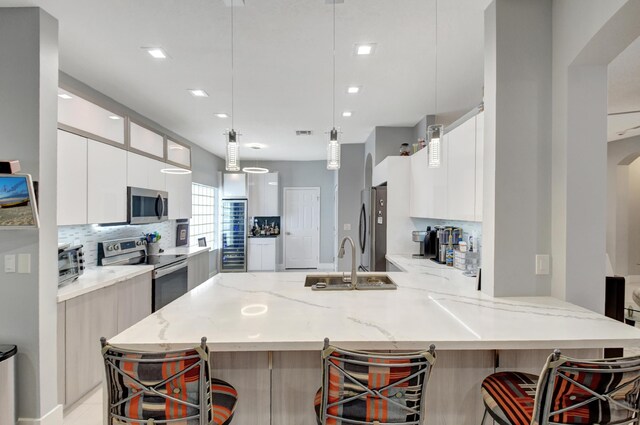 kitchen with light stone countertops, appliances with stainless steel finishes, a breakfast bar, sink, and decorative light fixtures