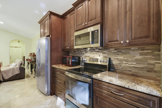 kitchen with tasteful backsplash, light stone countertops, light tile patterned floors, and appliances with stainless steel finishes