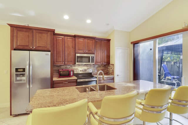 kitchen featuring sink, decorative backsplash, light stone counters, appliances with stainless steel finishes, and a kitchen bar