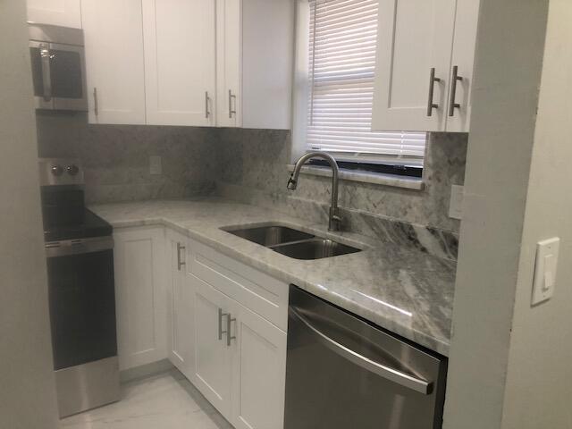 kitchen with backsplash, sink, light stone countertops, white cabinetry, and stainless steel appliances