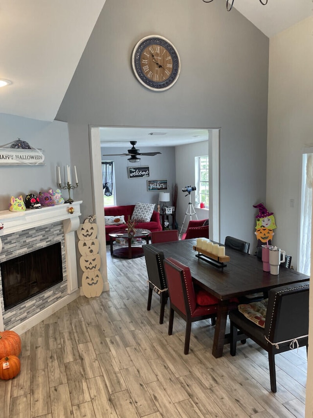 dining area with light wood-type flooring, a stone fireplace, ceiling fan, and lofted ceiling