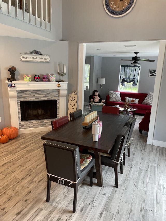 dining area featuring ceiling fan, light hardwood / wood-style floors, and a stone fireplace