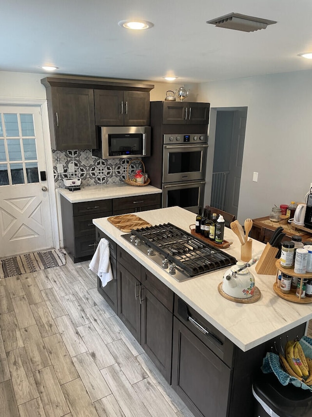 kitchen with dark brown cabinets, tasteful backsplash, stainless steel appliances, and light hardwood / wood-style flooring