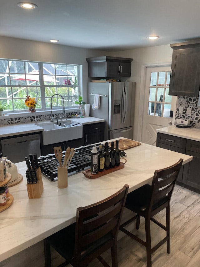 kitchen with light stone countertops, tasteful backsplash, stainless steel appliances, sink, and light hardwood / wood-style floors