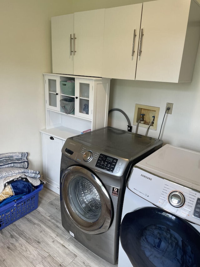 clothes washing area with cabinets, separate washer and dryer, and light hardwood / wood-style floors