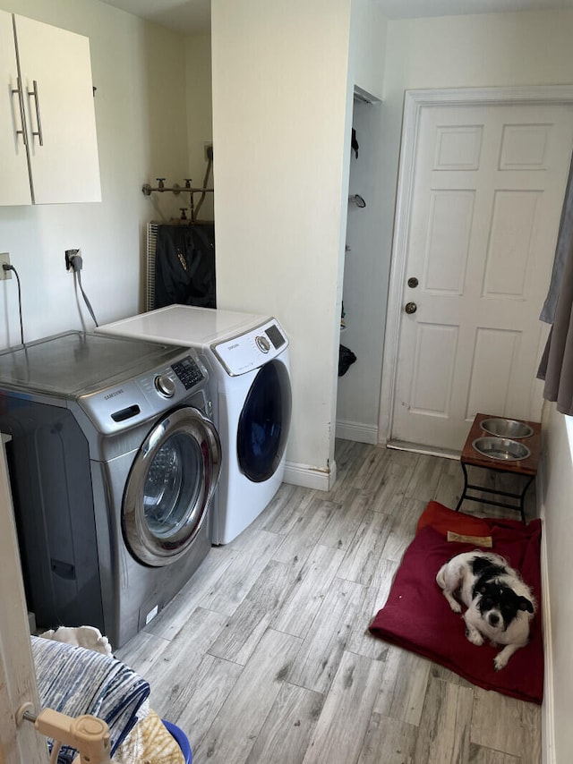 clothes washing area featuring cabinets, light wood-type flooring, and washing machine and clothes dryer