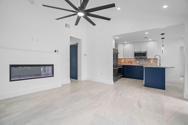 kitchen with high vaulted ceiling, blue cabinets, hanging light fixtures, appliances with stainless steel finishes, and white cabinetry