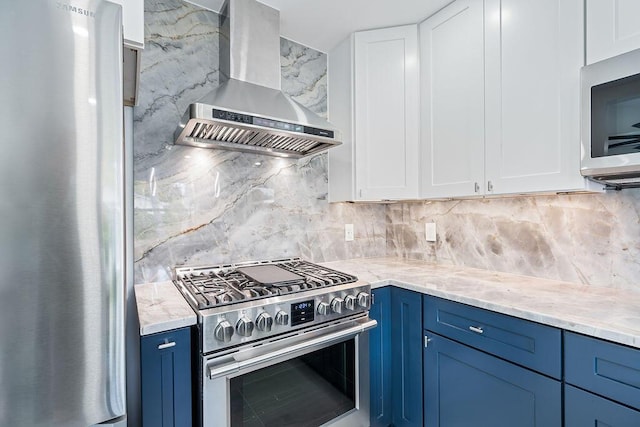 kitchen with wall chimney range hood, blue cabinets, decorative backsplash, white cabinets, and appliances with stainless steel finishes