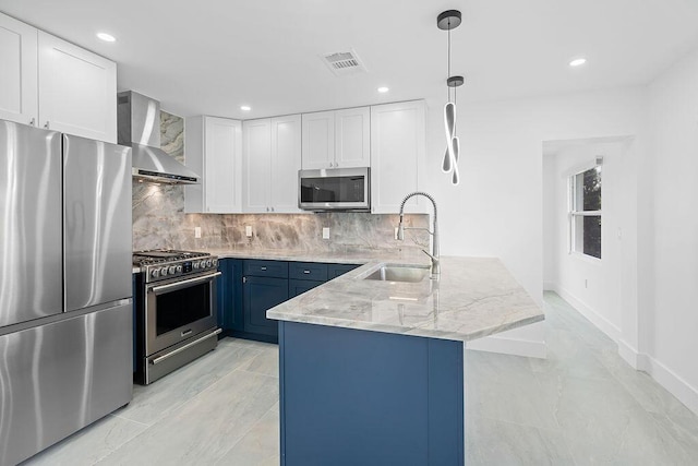 kitchen with stainless steel appliances, blue cabinets, wall chimney range hood, decorative light fixtures, and white cabinets