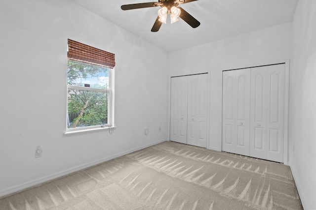 unfurnished bedroom featuring ceiling fan, carpet floors, and two closets