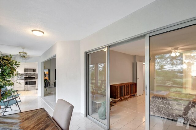 doorway featuring ceiling fan, light tile patterned floors, and a wealth of natural light