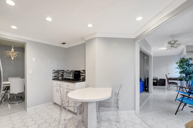 kitchen featuring light tile patterned floors, backsplash, a breakfast bar area, white cabinets, and ceiling fan with notable chandelier