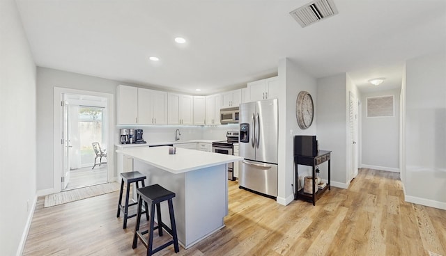 kitchen featuring a kitchen bar, appliances with stainless steel finishes, a center island, light hardwood / wood-style floors, and white cabinetry