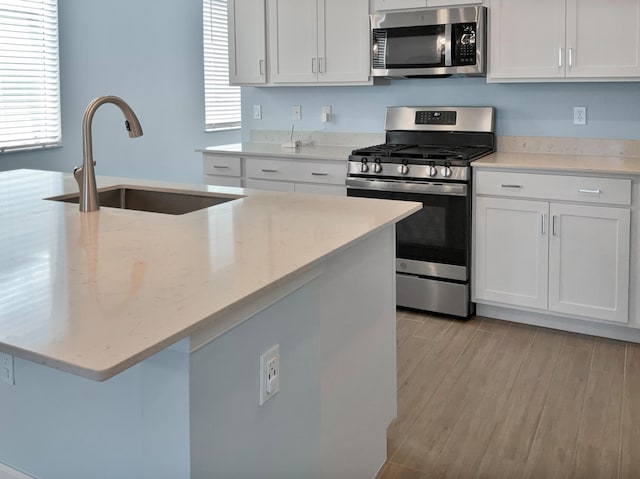 kitchen with light stone countertops, sink, appliances with stainless steel finishes, white cabinets, and light wood-type flooring