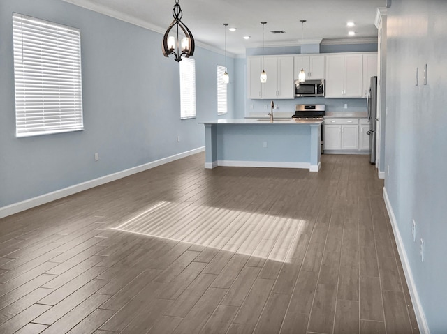 kitchen with a kitchen island with sink, white cabinets, crown molding, hanging light fixtures, and stainless steel appliances