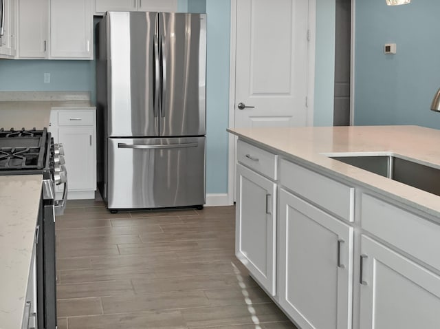 kitchen with white cabinets, sink, hardwood / wood-style flooring, light stone counters, and stainless steel appliances