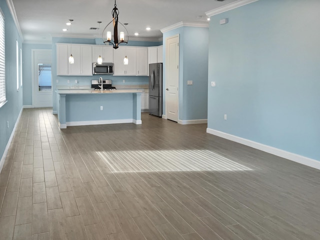 kitchen with appliances with stainless steel finishes, a kitchen island with sink, sink, white cabinets, and hanging light fixtures