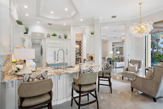 kitchen with light stone countertops, ornamental molding, a tray ceiling, sink, and white cabinets