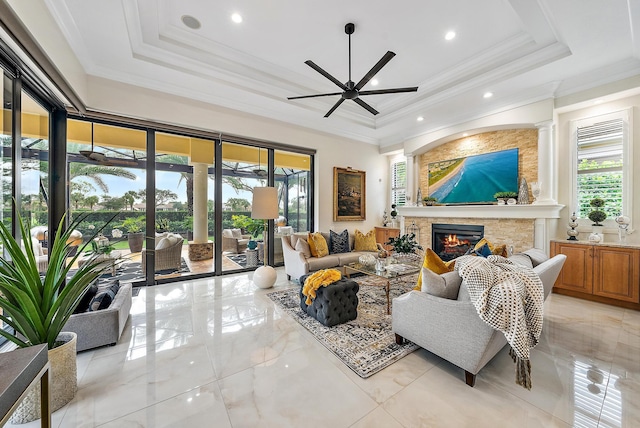 living room with a raised ceiling, ceiling fan, a stone fireplace, and a wealth of natural light