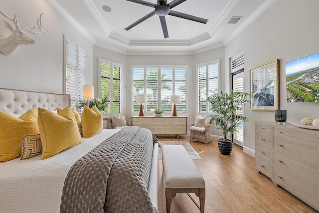 bedroom with ceiling fan, a raised ceiling, crown molding, and light hardwood / wood-style flooring