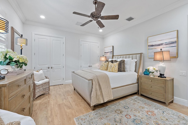 bedroom featuring ceiling fan, light hardwood / wood-style floors, ornamental molding, and two closets