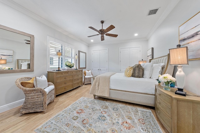 bedroom featuring ornamental molding, light hardwood / wood-style flooring, ceiling fan, and multiple closets